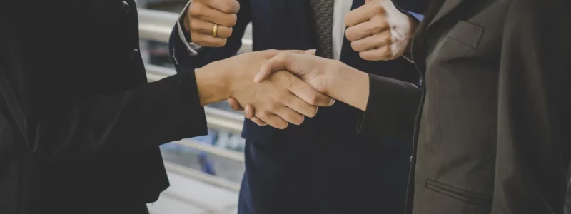 2 femmes d'affaire se serrant la main devant un intermédiaire avec les pouces levés.